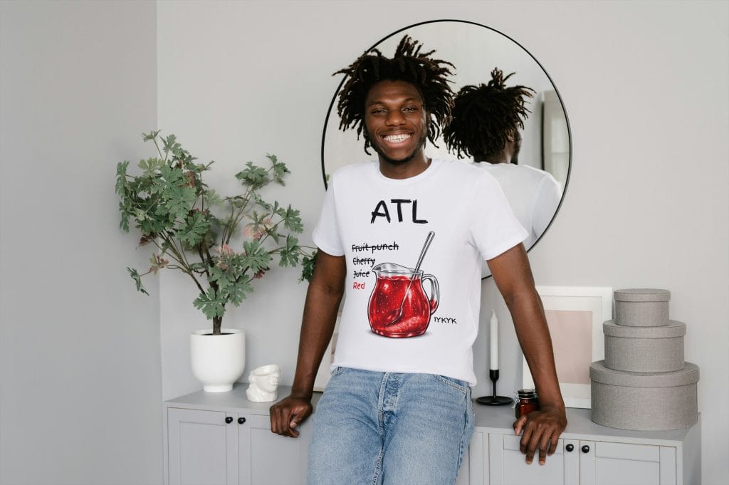 Smiling young man with dreadlocks wearing a white graphic t-shirt in a contemporary living space.