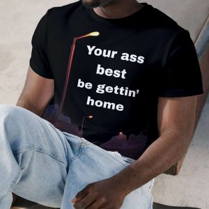 Young man sitting with skateboard, wearing a black t-shirt with humorous text, casual style.