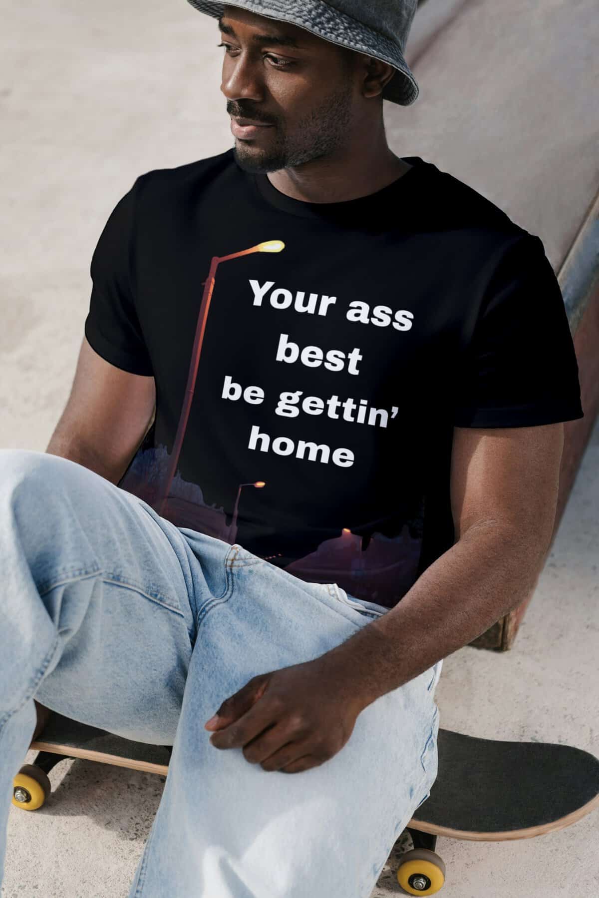 Young man sitting with skateboard, wearing a black t-shirt with humorous text, casual style.