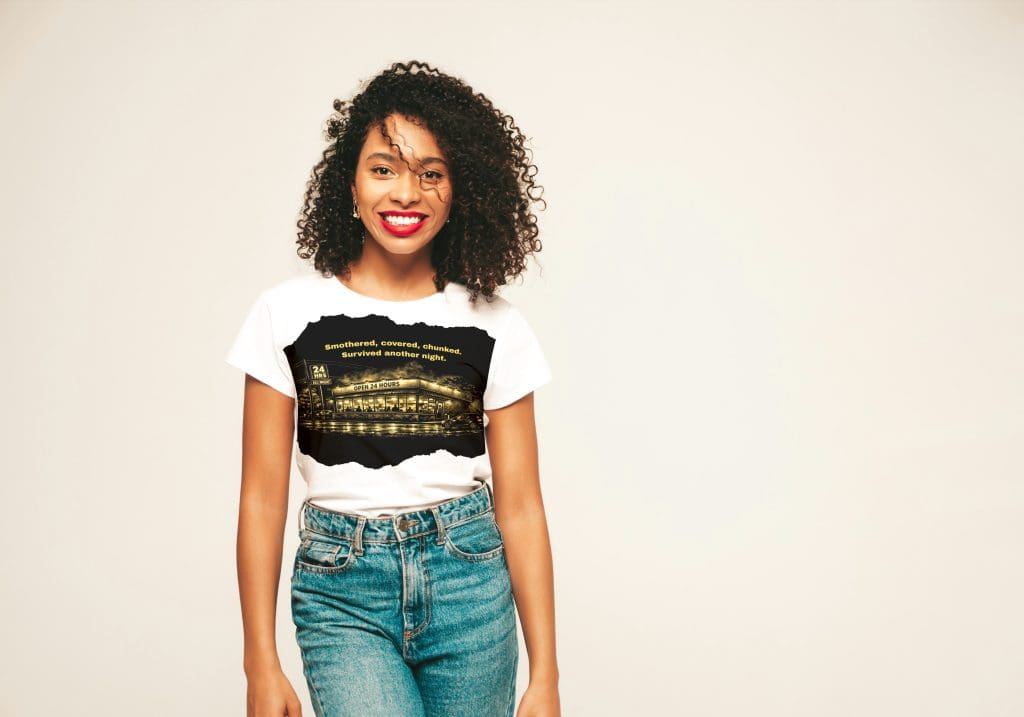 Smiling woman with curly hair wearing a white T-shirt and jeans, standing against a plain background.