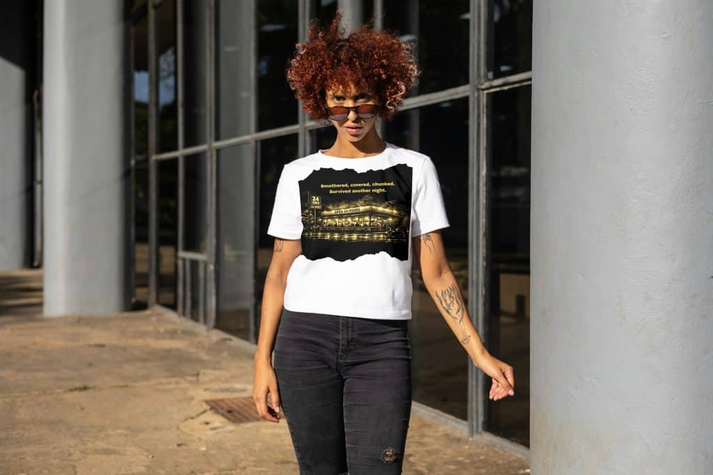Woman with curly hair wearing a graphic T-shirt and black jeans outside a modern building.
