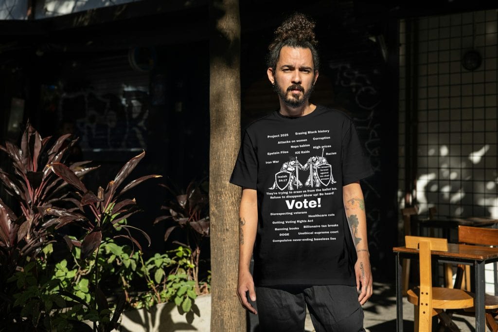 Man with curly hair and tattoos wearing a black Cousins Dozens T-shirt outdoors.