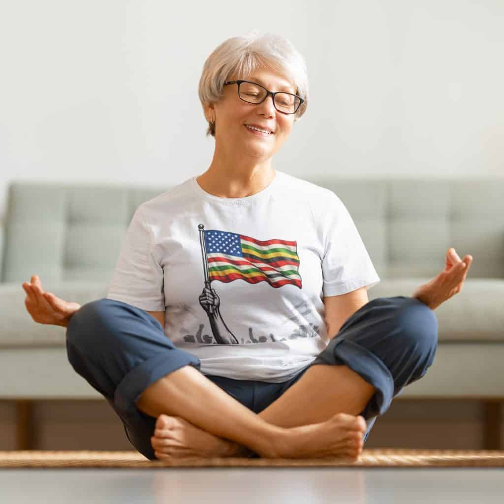 Woman practicing yoga with American flag t-shirt, sitting cross-legged at home.