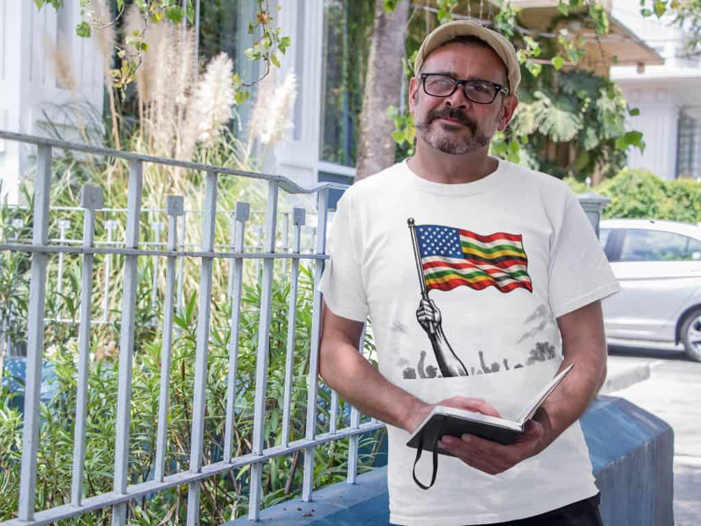 Man reading outdoors wearing a T-shirt with American flag design, casual setting.