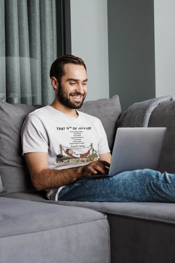 Happy man working on laptop while sitting on sofa in living room.