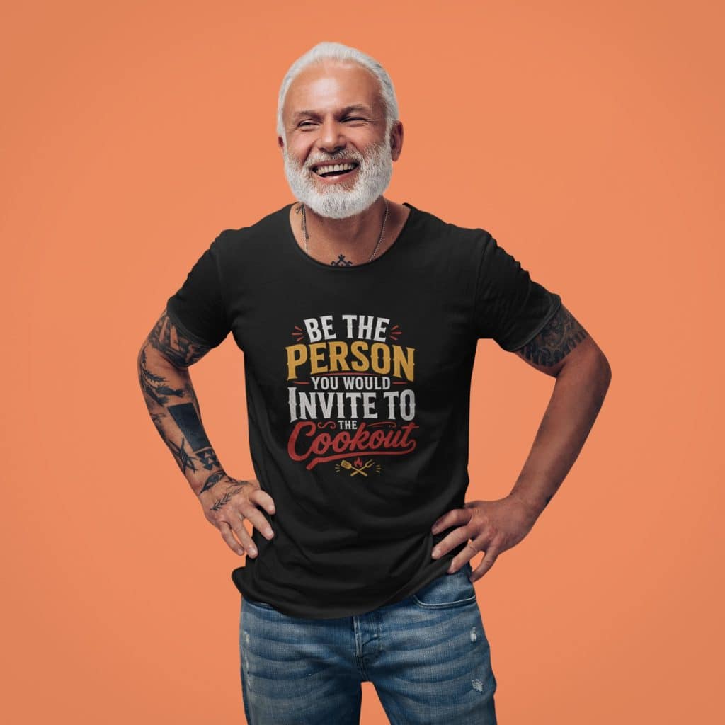 Smiling man with tattoos wearing a "Be the Person You'd Invite to Cookout" T-shirt.