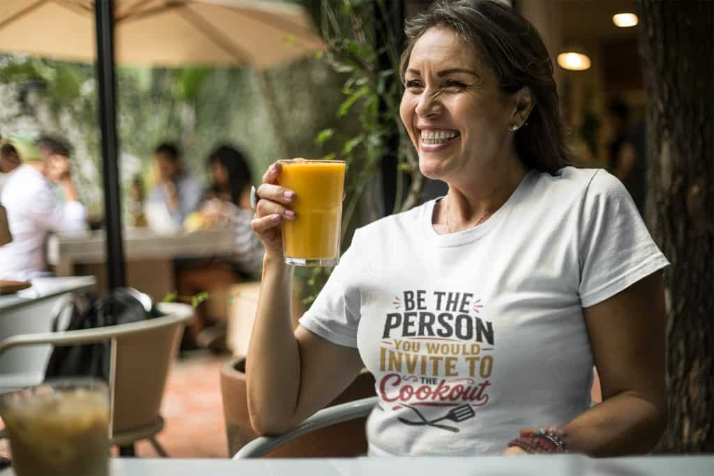 Woman enjoying fresh orange juice at outdoor café, smiling and relaxed.