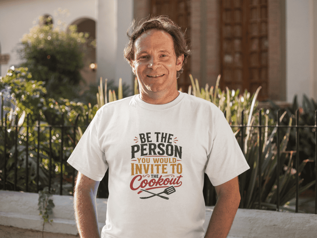 Man smiling outdoors wearing a "Be the person you would invite to the cookout" T-shirt.