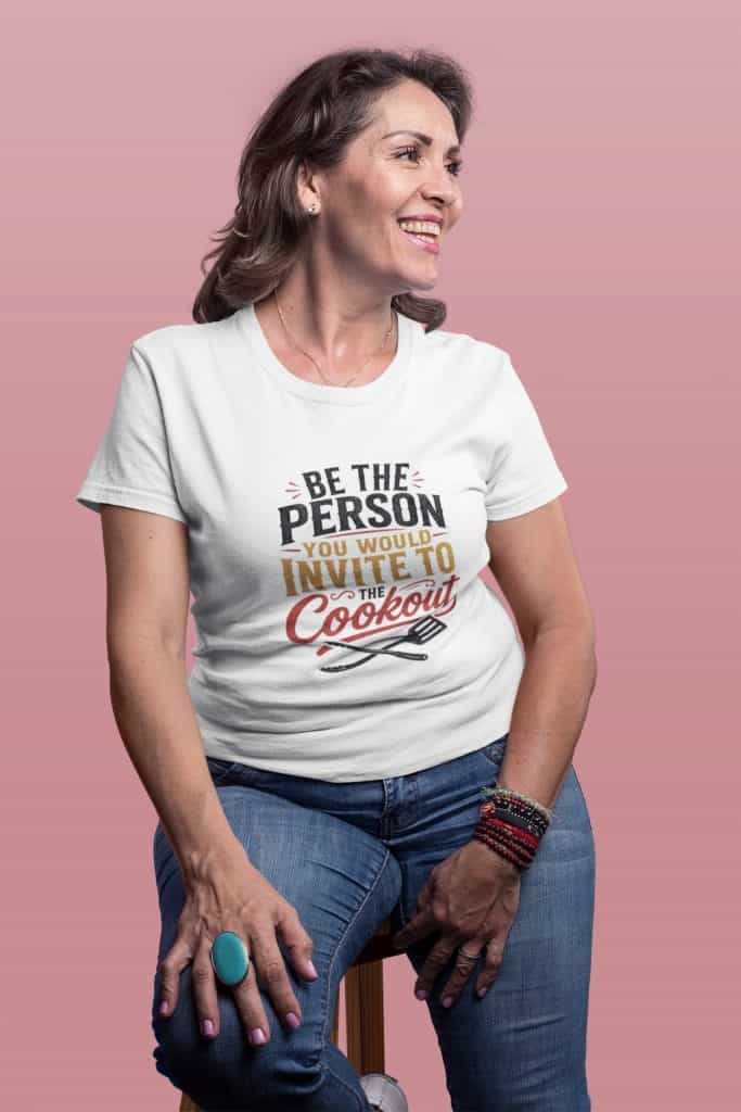 Smiling woman in casual outfit with "Be the Person You Invite to Cookout" t-shirt.